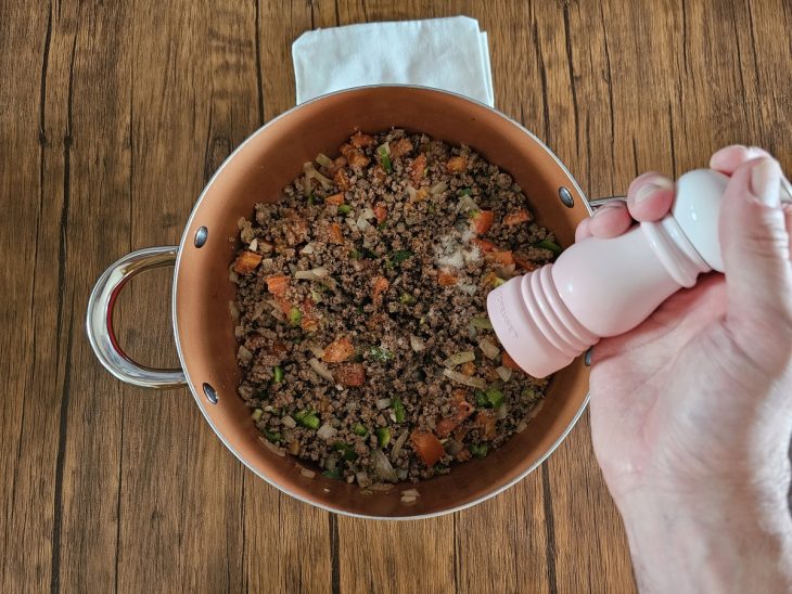 Uma panela contendo carne moída com manteiga, alho, tomate, pimentão e temperos.