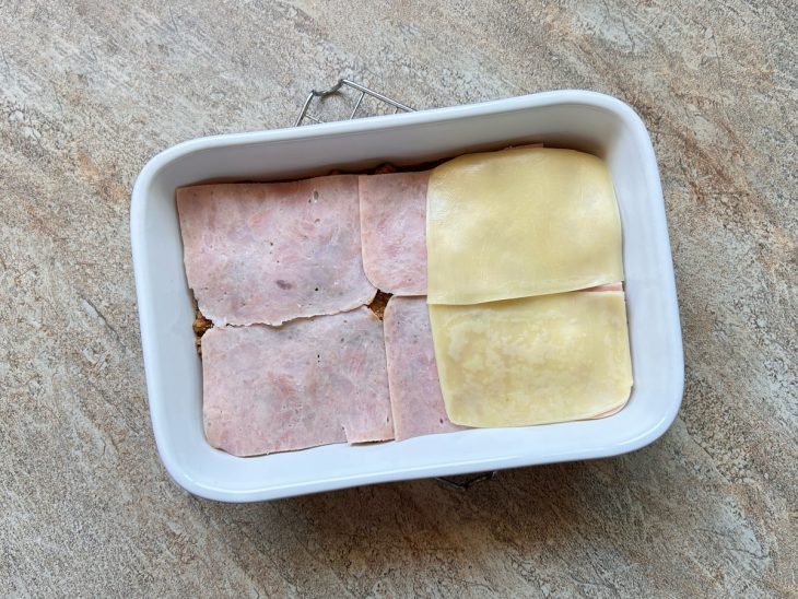 Na travessa, camada do presunto e queijo por cima da carne.