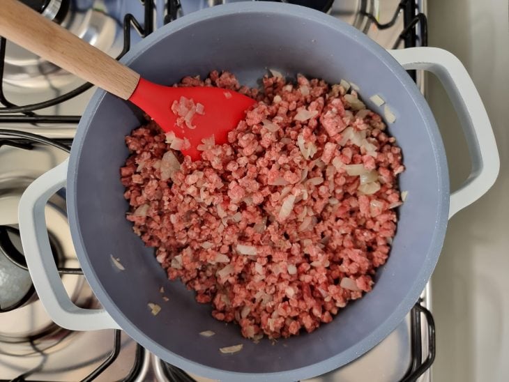 Panela com carne moída com coloração ainda avermelhada e temperos.