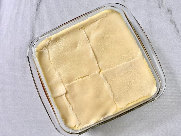 Escondidinho de carne moída montado em um recipiente de vidro e finalizado com fatias de queijo mussarela.