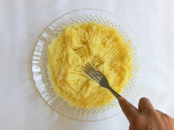 Batatas amassadas em um prato com auxílio de um garfo.