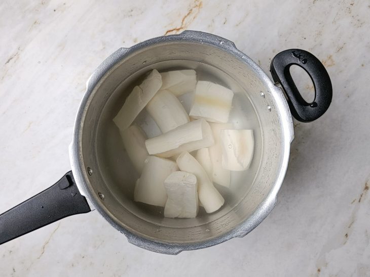 Pedaços de mandioca em uma panela de pressão com água.