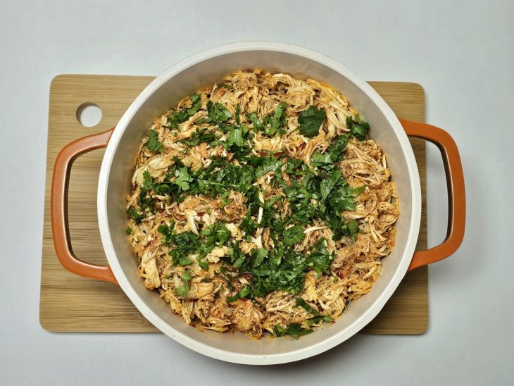 Na panela, coentro adicionado ao frango.