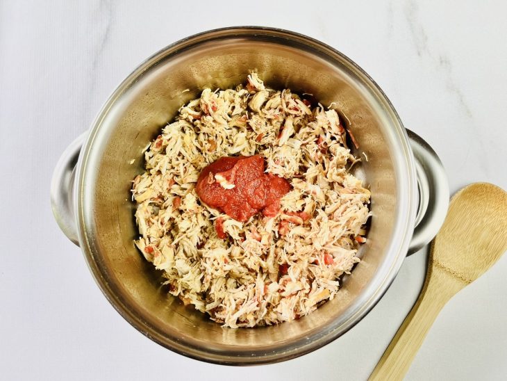 Panela com azeite, cebola picada, tomate picado, frango desfiado e extrato de tomate.