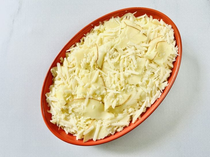 Purê de mandioquinha adicionado a travessa e queijos mussarela, parmesão e provolone salpicados por cima.