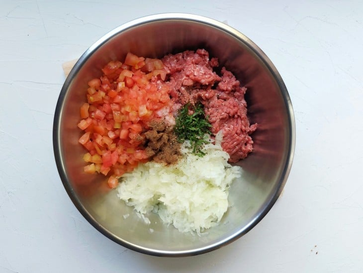 Um recipiente contendo carne moída, cebola, tomate, limão, sal, pimenta-do-reino, pimenta siria e hortelã.