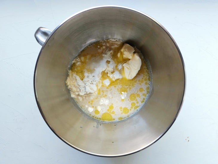Um recipiente contendo farinha, fermento seco, açúcar refinado, sal, manteiga, óleo e água.
