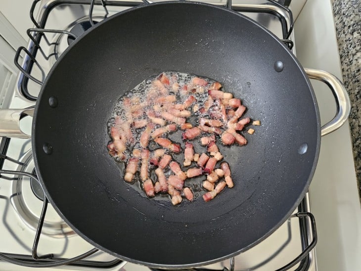 Uma frigideira com as tirinhas de bacon sendo fritas.