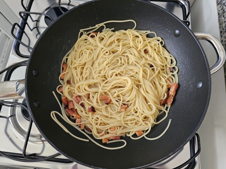 Uma frigideira com bacon e macarrão cozido.