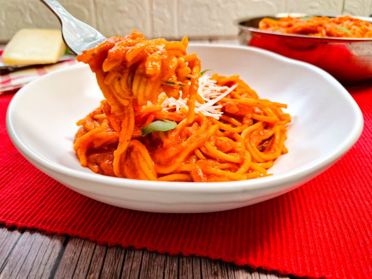 Macarrão pronto e porção servida em prato branco, frigideira ao fundo.