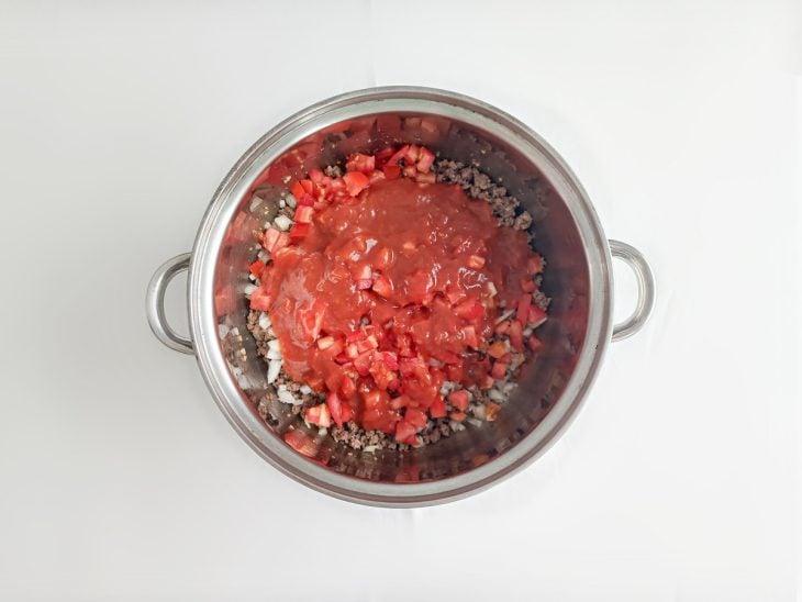 Cebola, tomate e molho de tomate adicionados na panela com carne moída.