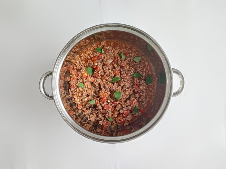 Molho de carne moída pronto com folhas de manjericão para finalizar.