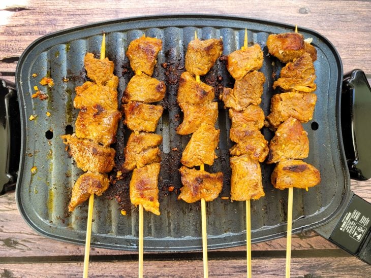 Espetinhos de carne sobre uma chapa.