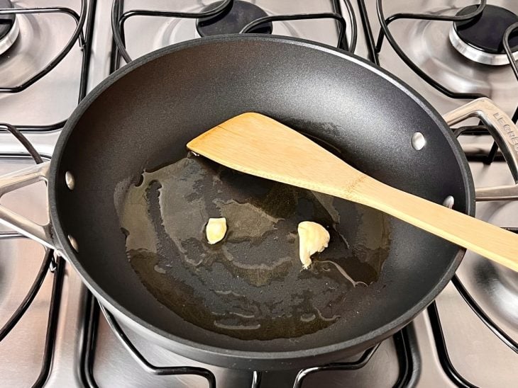 Uma frigideira contendo azeite refogando o dente de alho.