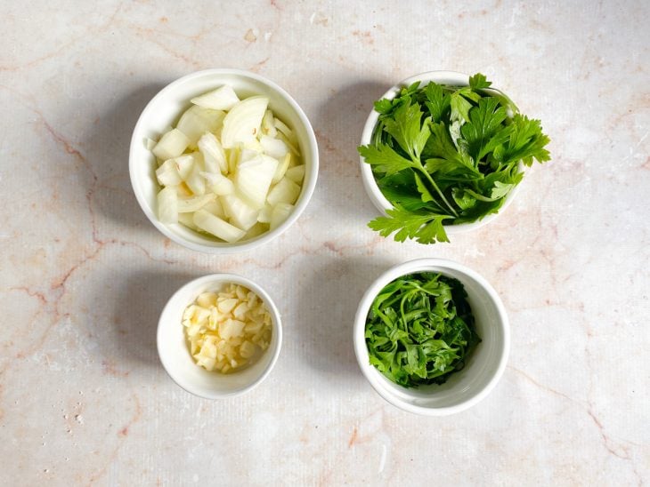 Alho, cebola, salsa e coentro em recipientes separados.