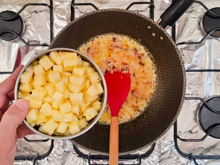 Cubos de abacaxi sendo incorporados ao refogado.
