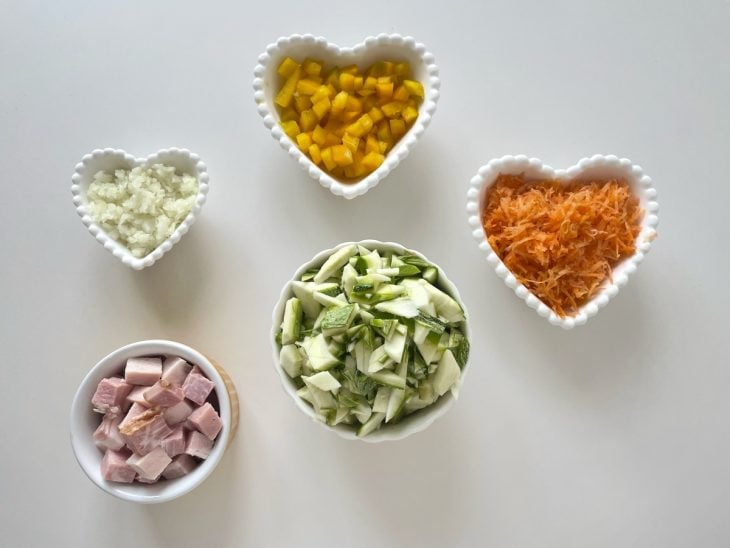 Abobrinha sendo ralada e demais ingredientes sendo picados.