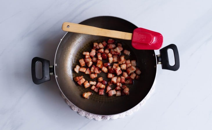 Uma frigideira com cubinhos de bacon fritos.