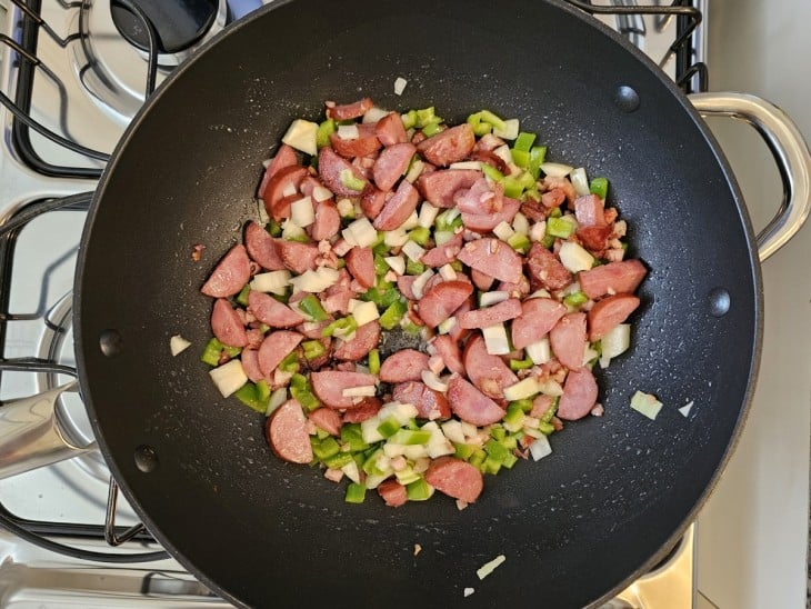 Uma frigideira com bacon, calabresa e legumes refogados.