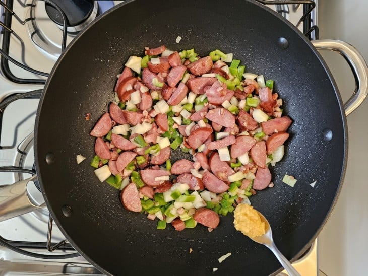 Uma frigideira com bacon, calabresa, alho e legumes refogados.