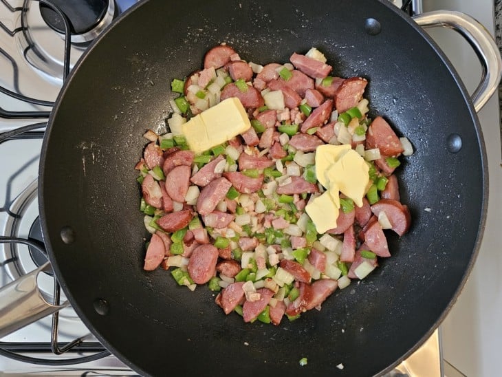 Uma frigideira com bacon, calabresa, legumes refogados e manteiga.