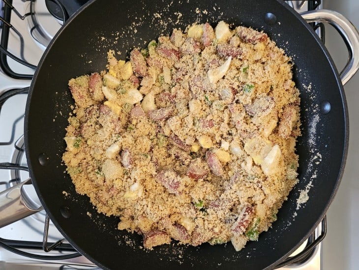 Uma frigideira com bacon, calabresa, legumes refogados e farinha de milho.