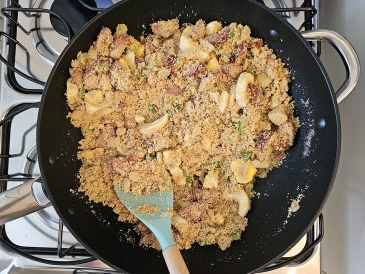 Uma frigideira com bacon, calabresa, legumes e farinha de milho refogados.