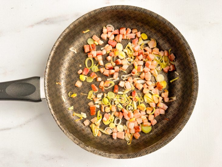 Na frigideira, o bacon e o alho poró.