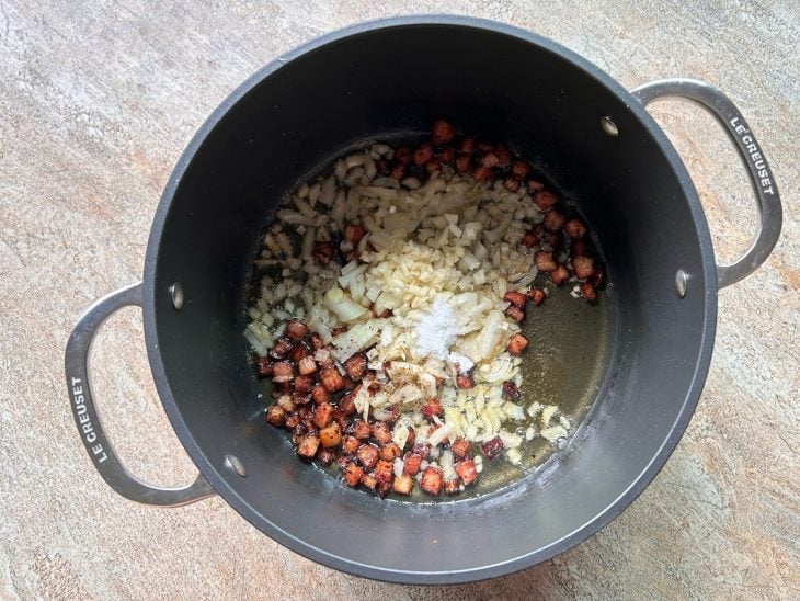 Uma panela com manteiga, bacon, cebola, alho, pimenta-do-reino e sal.