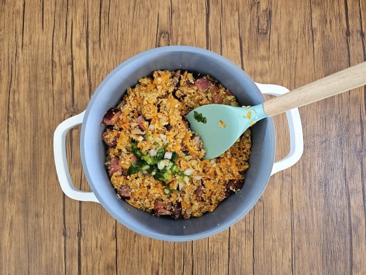 Cenoura, bacon, calabresa, cebola, farinha e cebolinha misturados em uma panela cinza com alças na cor branca.