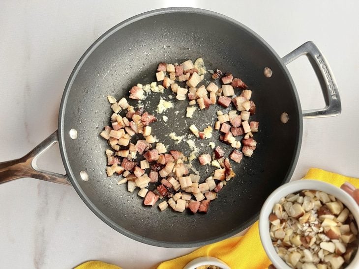 Uma frigideira fritando o bacon e cebola.