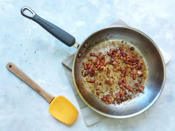 Bacon frito na frigideira com espátula ao lado.