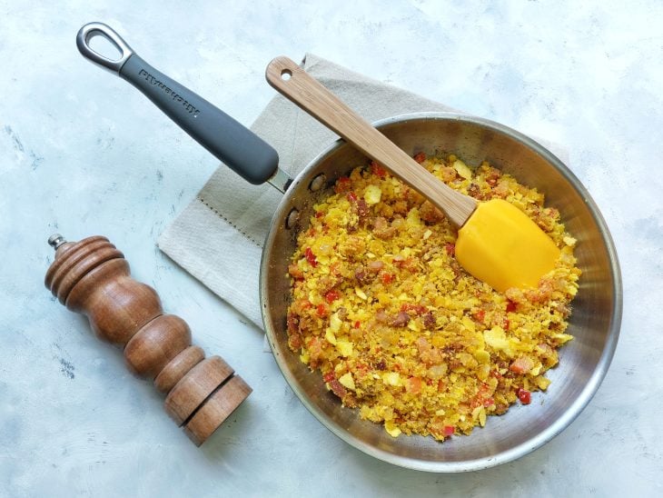 Frigideira com farofa, espátula e ralador de sal e pimenta-do-reino ao lado.