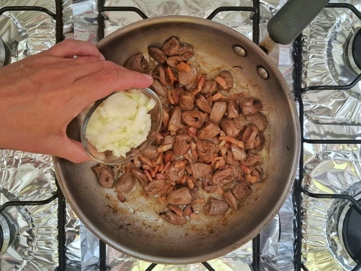 Uma panela com o coração de galinha refogando e a adição de cebola.