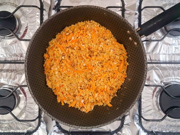Na frigideira, a cenoura ralada, as nozes picadas, as uvas-passa e a pimenta dedo-de-moça adicionados junto a farinha de mandioca.