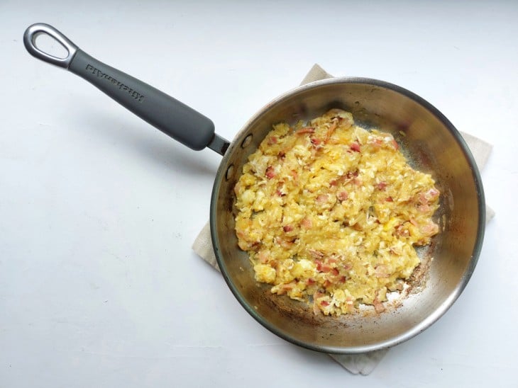Frigideira de ferro com a mistura de bacon, cebola, alho e ovos.