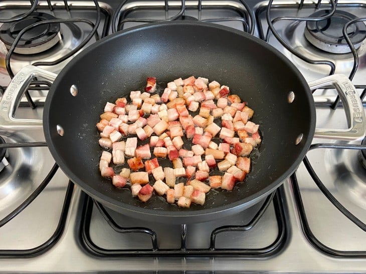 Uma frigideira com bacon em cubinhos fritos.