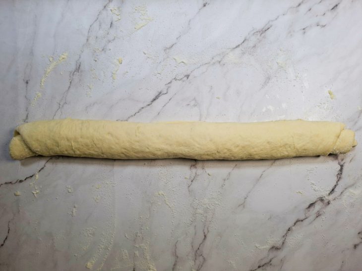 Massa sendo enrolada formando um rocambole uniforme.