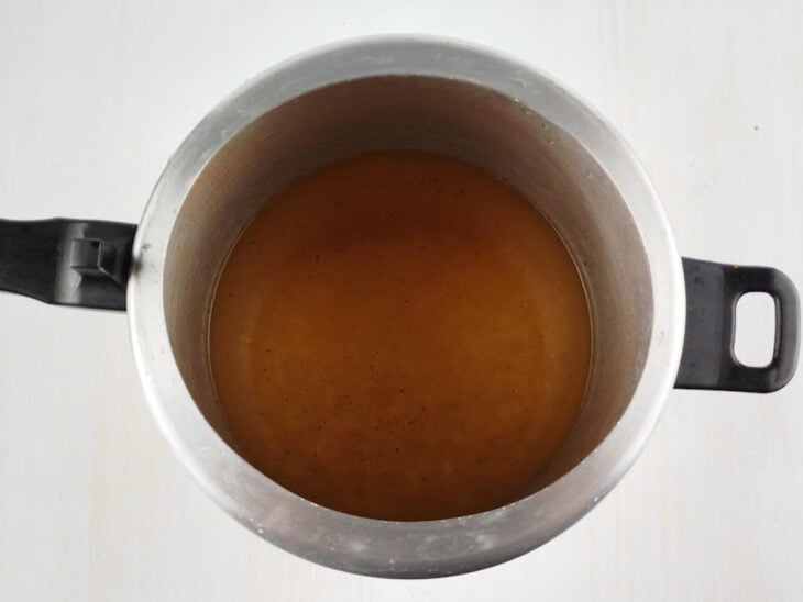 Caldo coado das cascas sendo despejado na panela de pressão com o feijão branco e a folha de louro.