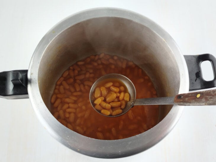 Pedaços de cenoura sendo adicionados ao feijão já cozido e macio na panela aberta.