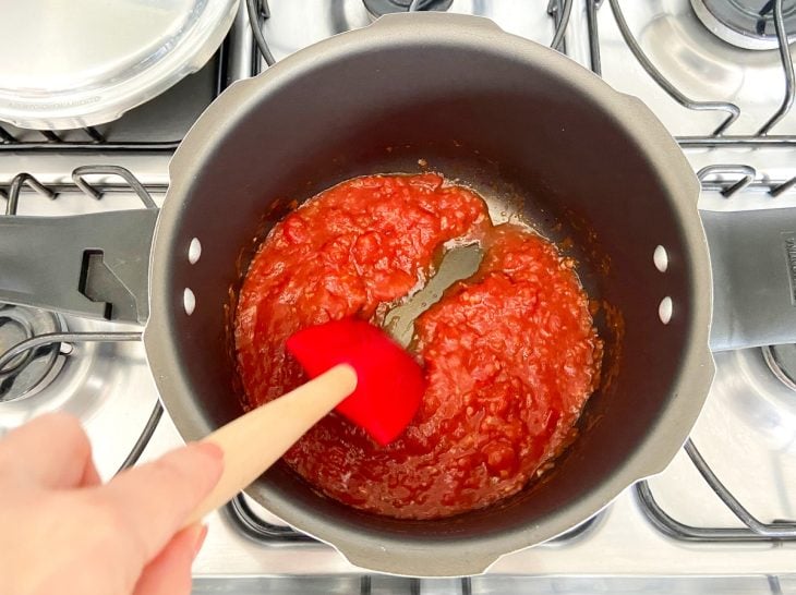 Uma panela de pressão refogando alho, cebola, temperos e molho de tomate.