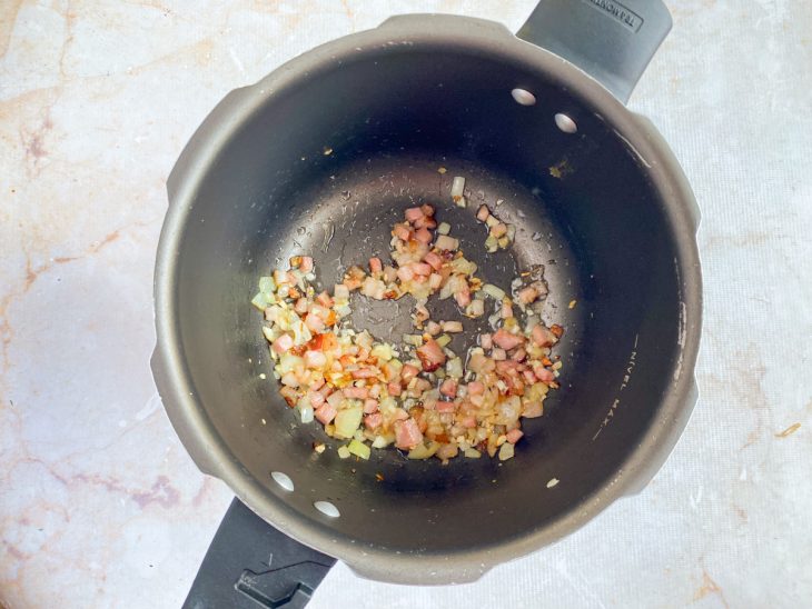 Na panela de pressão, o bacon, o alho, e a cebola dourados.