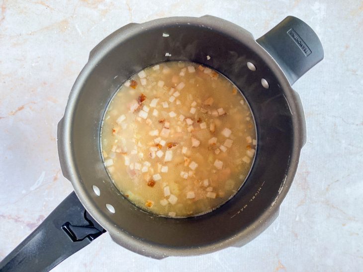Na panela de pressão, feijão já cozido e com bastante caldo.