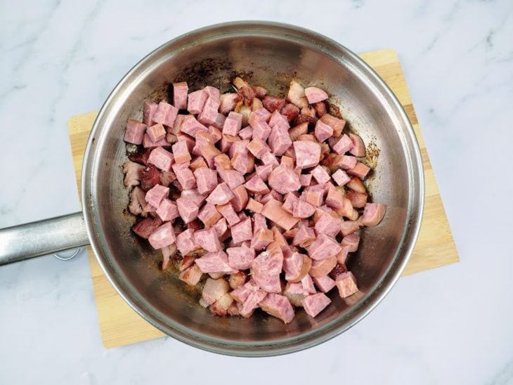 Uma frigideira com bacon e calabresa fritando.