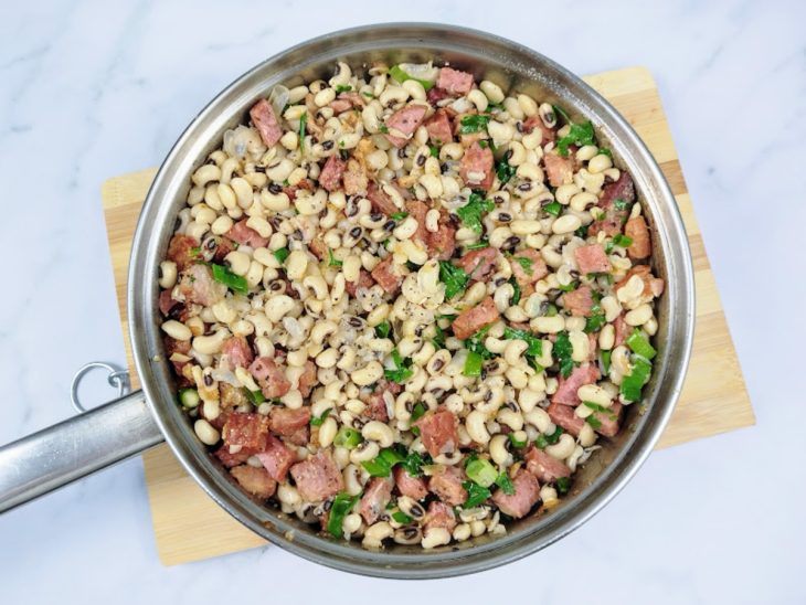 Uma panela de pressão com feijão, bacon, calabresa e temperos misturados.