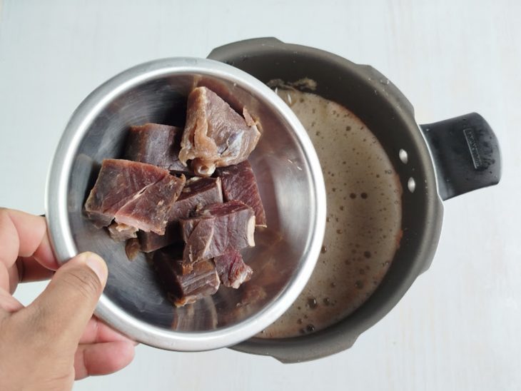 Mistura batida e cubos de charque adicionados na panela de pressão.