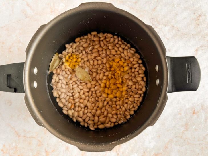 Feijão lavado sendo colocado na panela com água e louro.