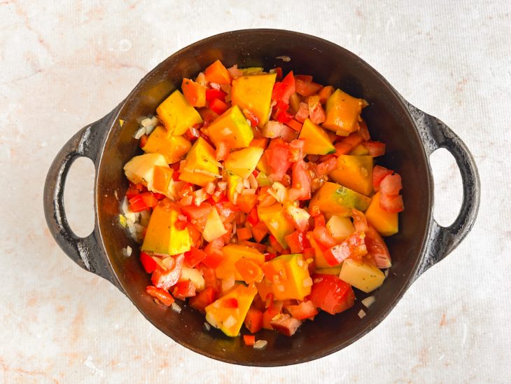 Temperos e tomate misturados aos legumes na panela.