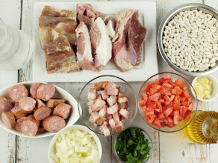 Ingredientes organizados sobre a bancada com carnes e legumes picados.