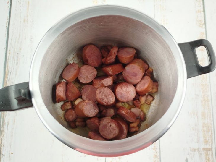 Linguiça calabresa e bacon dourando na panela de pressão com óleo quente.